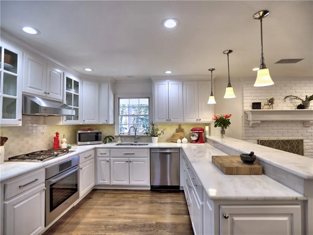 Kitchen with sink, white cabinetry, decorative light fixtures, appliances with stainless steel finishes, and kitchen peninsula