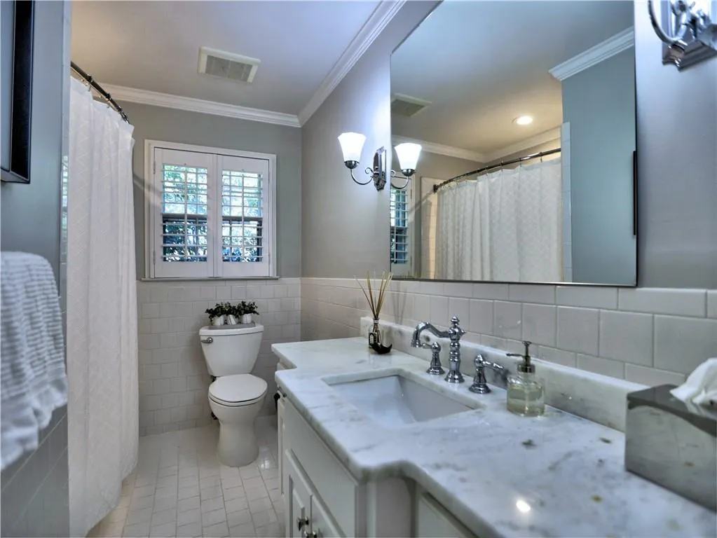 Bathroom featuring tile patterned flooring, tile walls, vanity, ornamental molding, and toilet