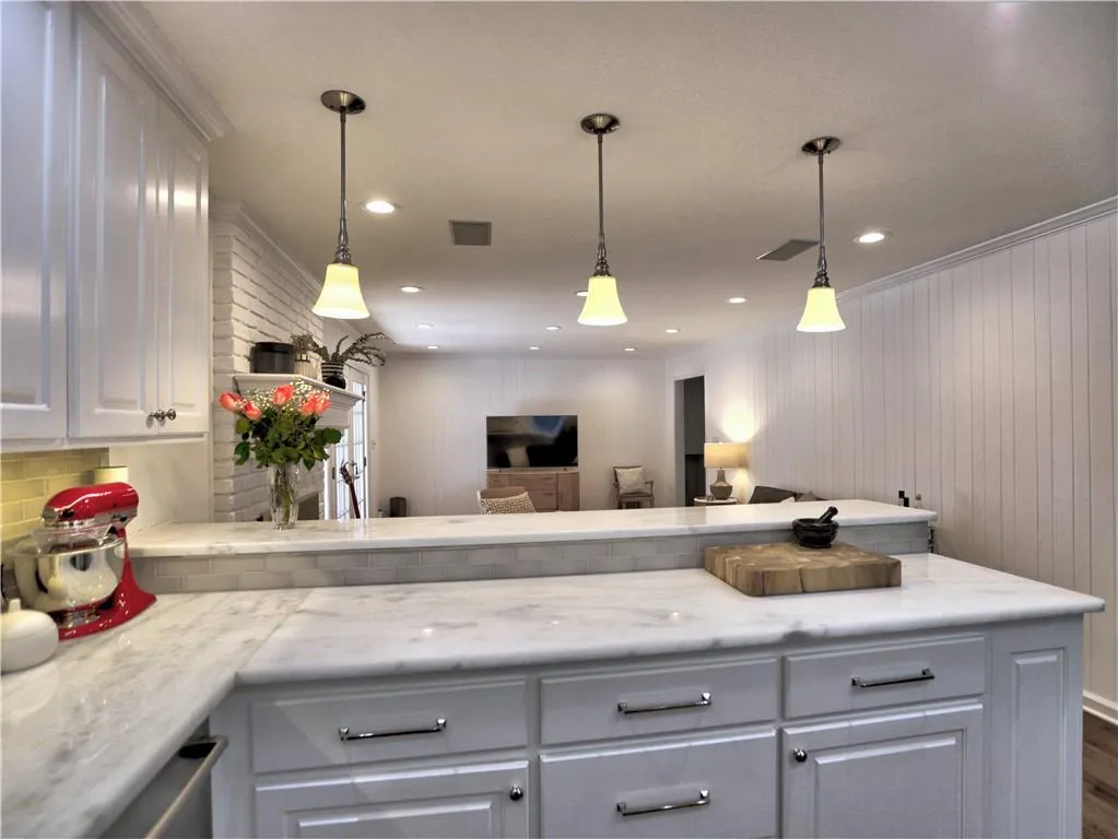 Kitchen featuring white cabinetry, decorative light fixtures, light stone countertops, and backsplash