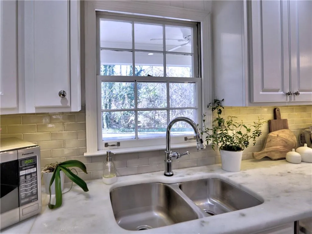 Kitchen with white cabinetry, light stone countertops, sink, and backsplash