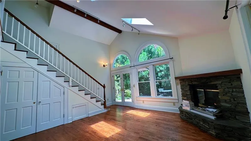 Unfurnished living room with track lighting, a skylight, stairs, wood finished floors, and a stone fireplace