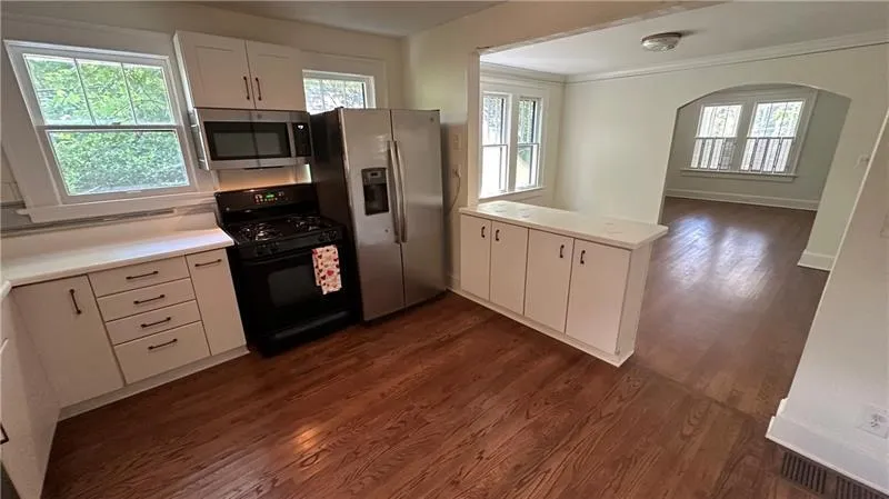 Kitchen with stainless steel appliances, a peninsula, dark wood-type flooring, white cabinets, and light countertops