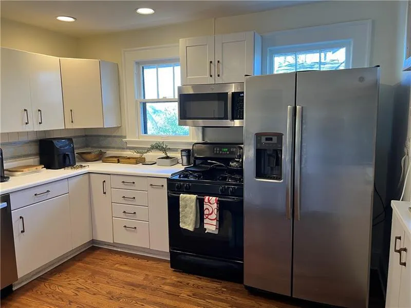 Kitchen featuring appliances with stainless steel finishes, wood finished floors, decorative backsplash, light countertops, and white cabinets