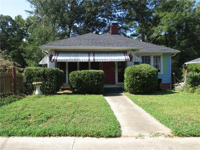 Front exterior with a dark shingle roof, red entry door, white striped awning, and mature front yard landscaping