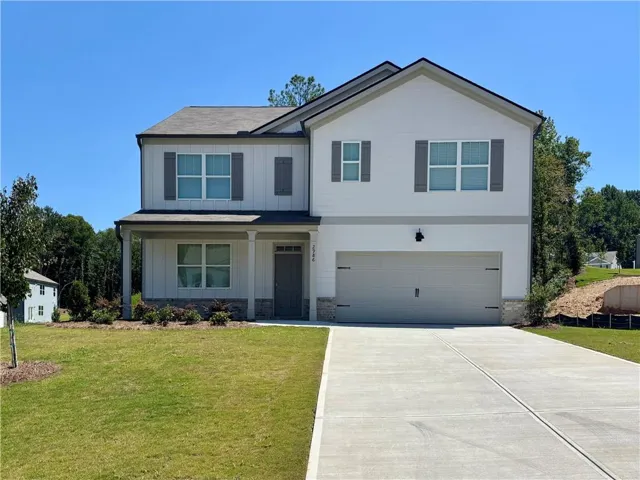 Two-story residence featuring a covered front porch, an attached garage, a paved driveway, and manicured landscaping
