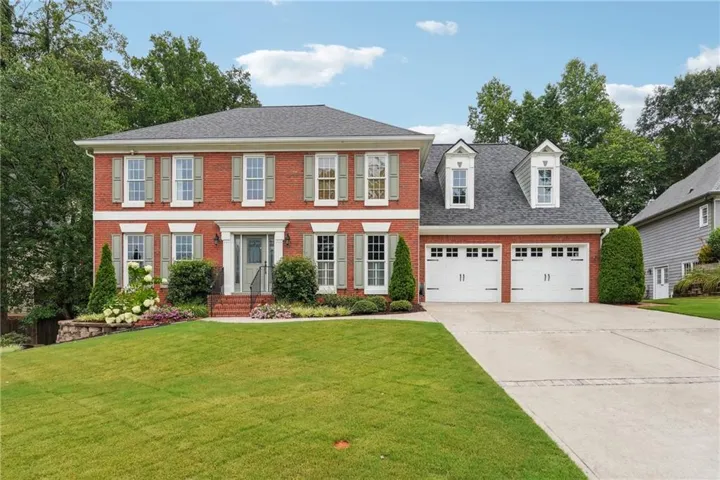 Brick exterior with gray shutters, a two-car garage with white doors, a concrete driveway, and mature landscaping