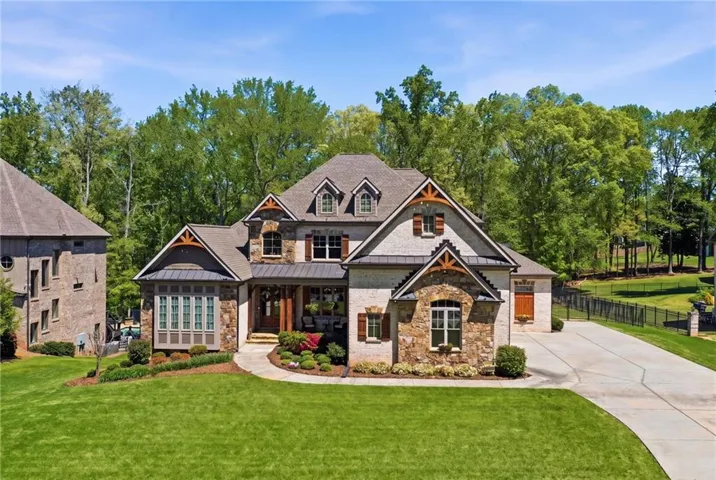Craftsman-style house featuring a standing seam roof, covered porch, driveway, stone siding, and view of wooded area