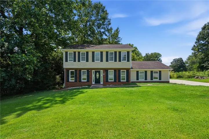 Two-story residence with brick and siding exterior, front lawn, and surrounding mature trees