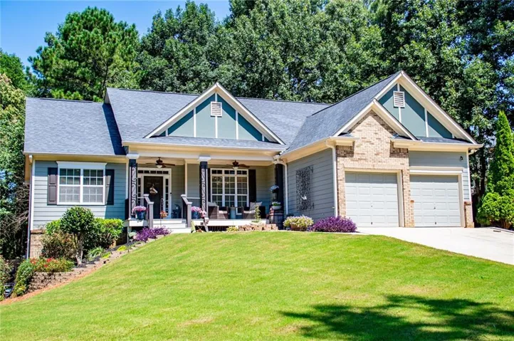 Siding exterior with brick accents, covered front porch, two-car garage, and mature trees