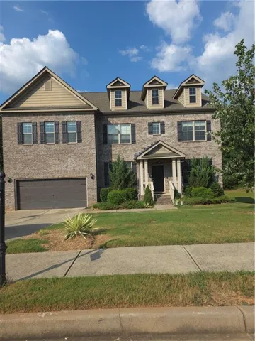 Two-story brick exterior with a front-facing gable, three dormer windows, attached garage, and a covered front entry