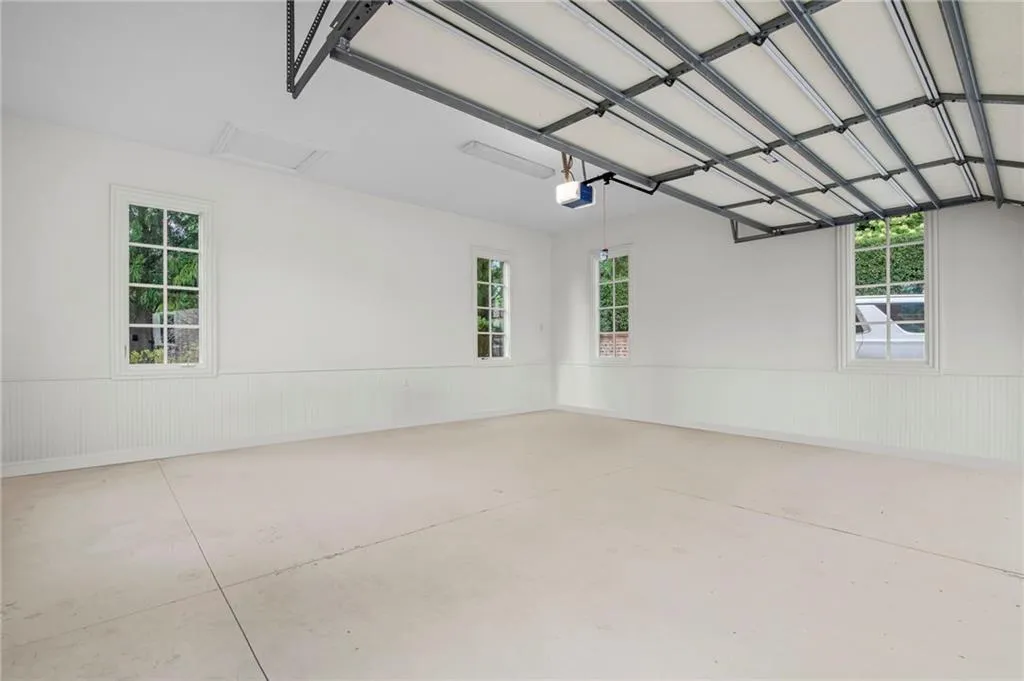Spacious garage featuring a concrete floor, three multi-pane windows, beadboard wainscoting, and an automatic garage door opener
