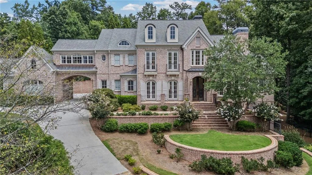 French-inspired brick exterior, multi-tiered landscaping, arched portico, dormer windows, and a circular driveway