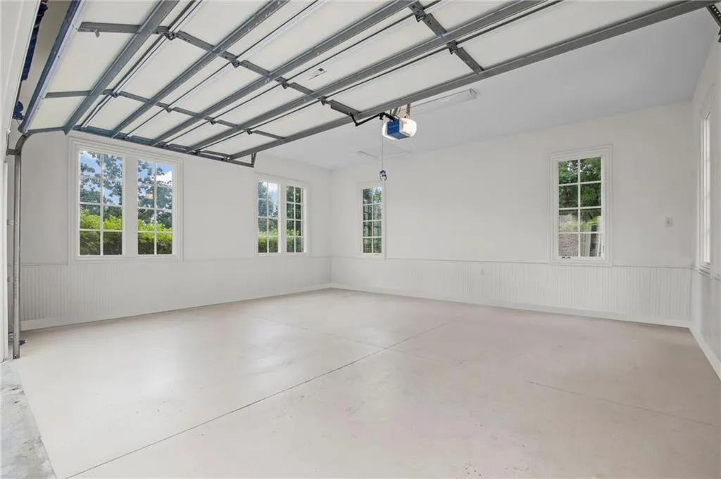 Spacious 2garage with multiple windows, beadboard wainscoting, a painted concrete floor, and an automatic garage door opener