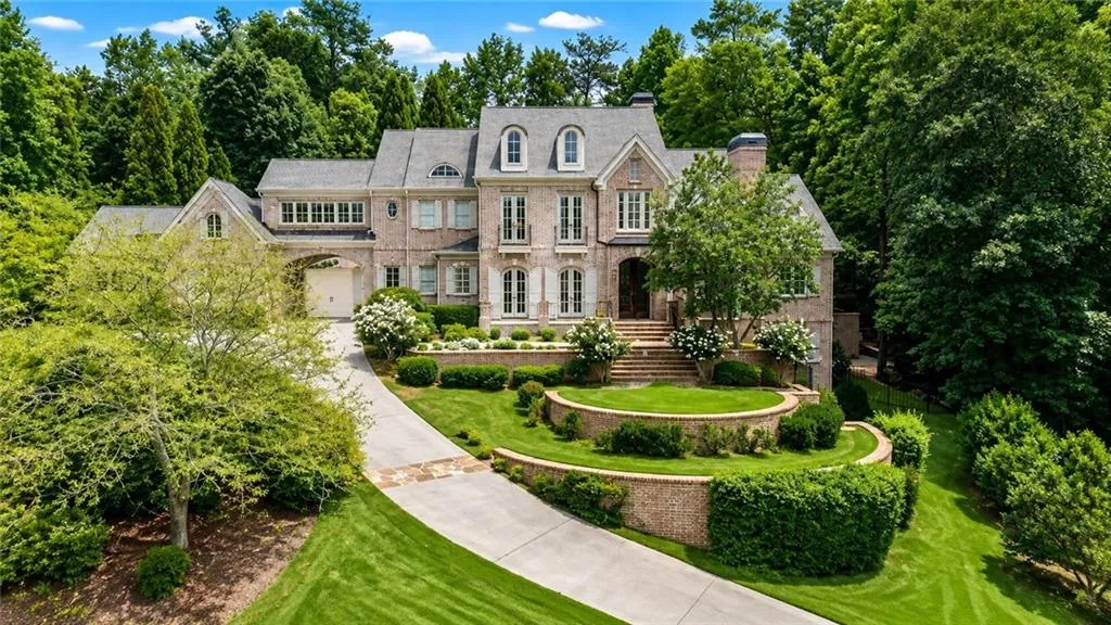 Brick exterior with multiple dormer windows, a circular driveway, and a terraced front yard with mature landscaping