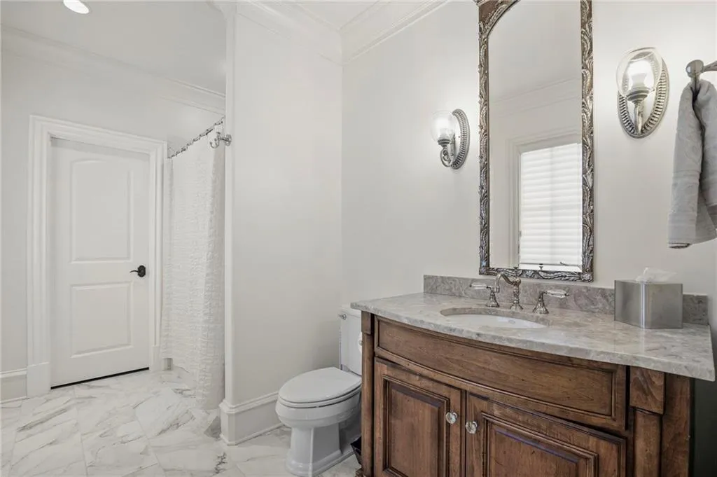 Secondary Bathroom 1 featuring a wood-finish vanity with a stone countertop, updated stone look tile floors, and wall-mounted sconces,  Bath/shower combo with walk-in closet access