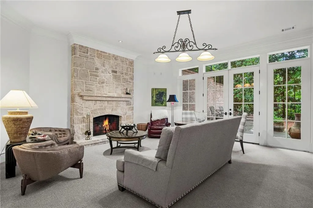 Stone fireplace, decorative light fixture, crown molding, French doors with transom windows, and light-colored carpet flooring