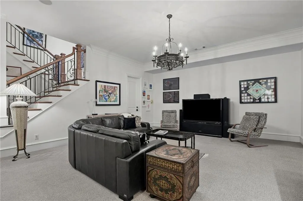 Carpeted living area with a wrought iron chandelier, crown molding, and a staircase featuring wood treads and wrought iron balusters