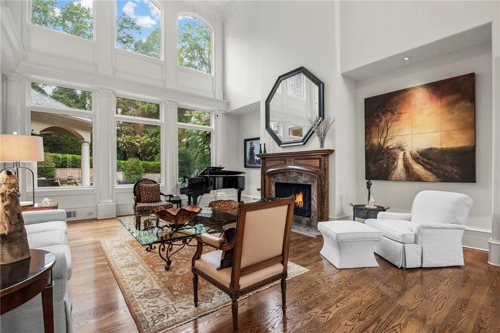 Hardwood flooring, fireplace with stone surround, wood mantel, tall arched windows, and recessed lighting