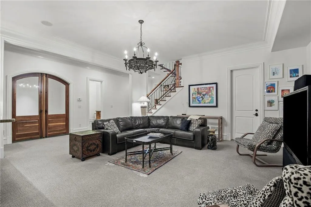 Arched wood-panel doors with frosted glass that leads to wine cellar, wrought iron chandelier, staircase with wood handrail and iron balusters, and white crown molding