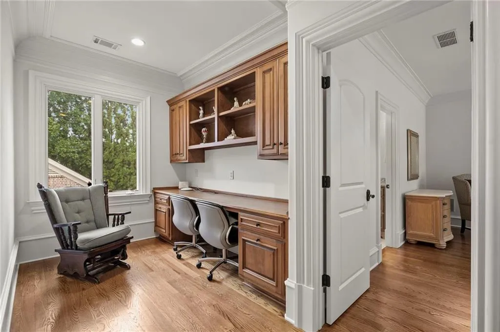 Dedicated home office space off landing  featuring custom wood cabinetry with open shelving, dual workspace with built-in desk surfaces, hardwood flooring, and abundant natural light from large double-pane windows
