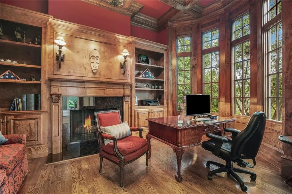 Hardwood flooring, custom built-in shelving, stone fireplace surround, wood-paneled walls, and large multi-pane windows