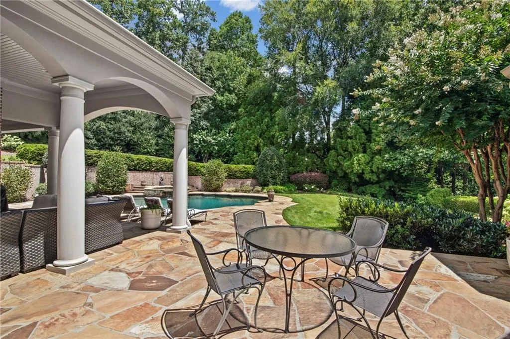 Covered patio with substantial columns, flagstone paving, and a clear-water swimming pool