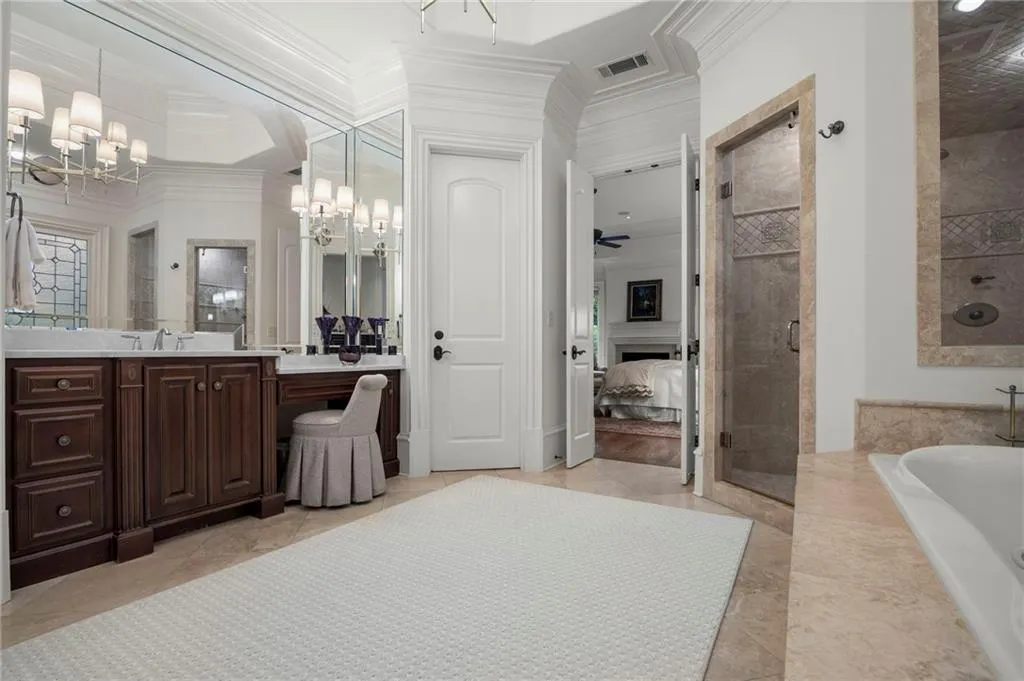 Double vanity with wood-finish cabinetry, built-in makeup area, extensive wall mirrors, and crown molding