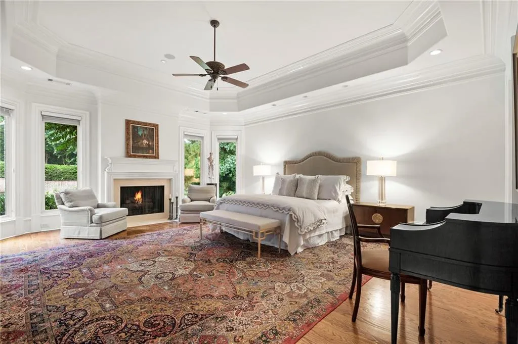 Hardwood flooring, tray ceiling with recessed lighting, ceiling fan, and a fireplace with a mantel