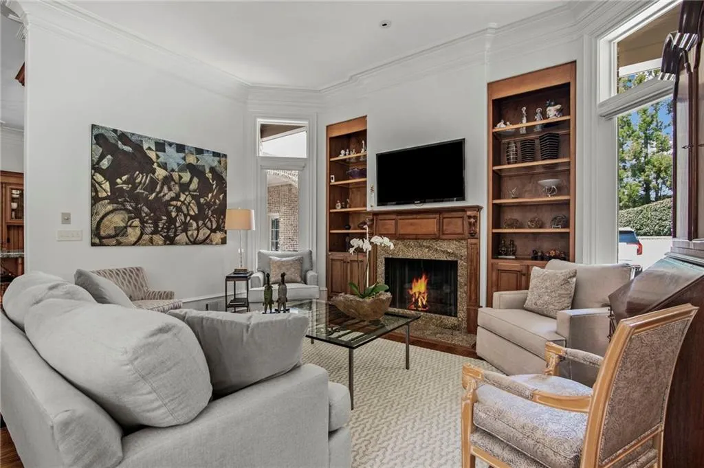 Living area with a fireplace featuring a detailed wood mantel and surround, built-in shelving, bay windows, and wood-finish flooring