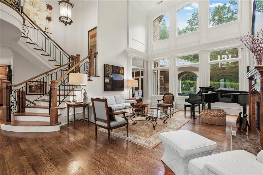 Grand double-height living space featuring hardwood flooring, a curved staircase with wrought iron balusters, a built-in fireplace with a stone surround, and extensive window walls with arched transoms