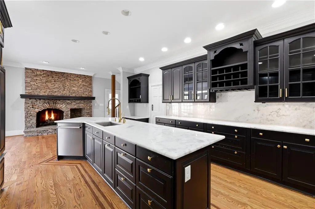 Kitchen with a kitchen island with sink, crown molding, glass fronted cabinets, light stone countertops, and a stone fireplace
