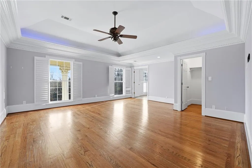 Unfurnished living room with ornamental molding, ceiling fan, light wood finished floors, healthy amount of natural light, and a tray ceiling