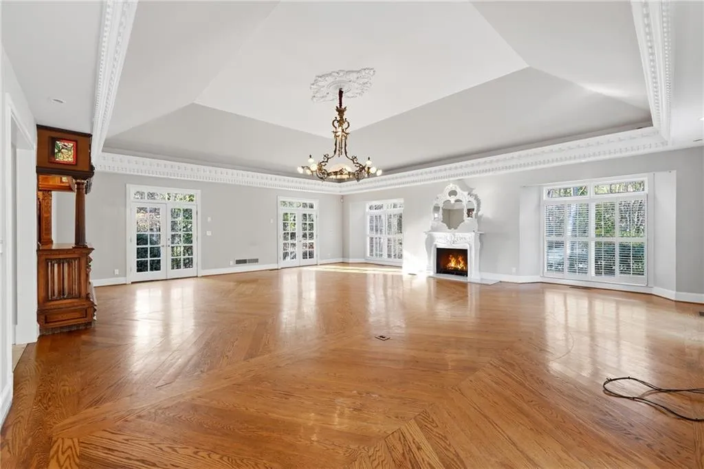 Unfurnished living room with parquet floors, suspended lighting, a fireplace with flush hearth, a raised ceiling, and healthy amount of natural light