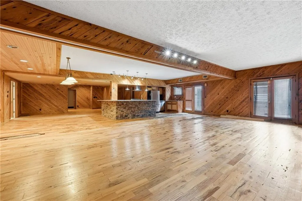 Unfurnished living room featuring light wood-style flooring, wood walls, and a textured ceiling