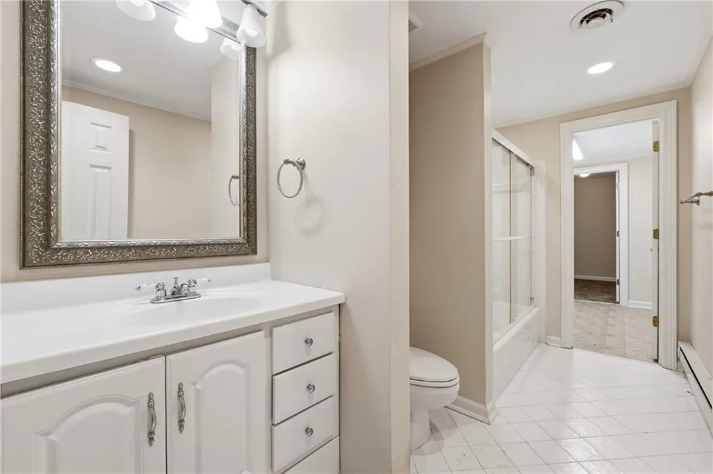 Full bathroom featuring vanity, recessed lighting, a baseboard radiator, bath / shower combo with glass door, and crown molding