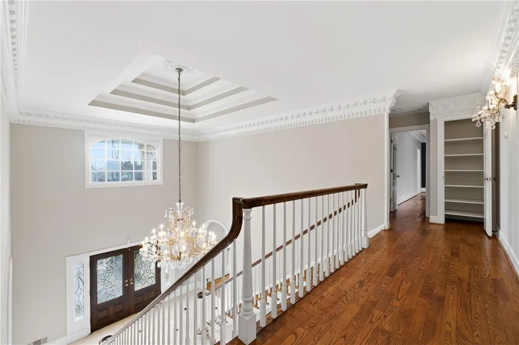 Hall featuring suspended lighting, ornamental molding, dark wood-style flooring, an upstairs landing, and a tray ceiling