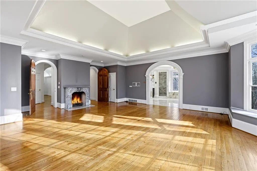Unfurnished living room with a fireplace with flush hearth, arched walkways, a tray ceiling, light wood-style floors, and ornamental molding