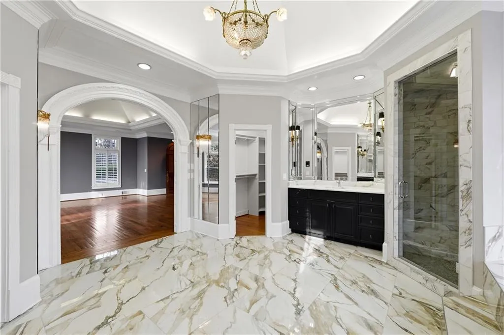 Full bath with ornamental molding, hanging lights, vanity, a marble finish shower, and light marble finish flooring
