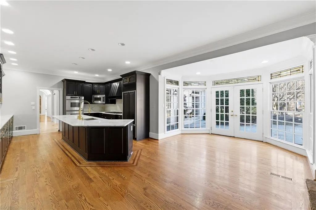 Kitchen with dark cabinets, light stone counters, french doors, an island with sink, and light wood-type flooring