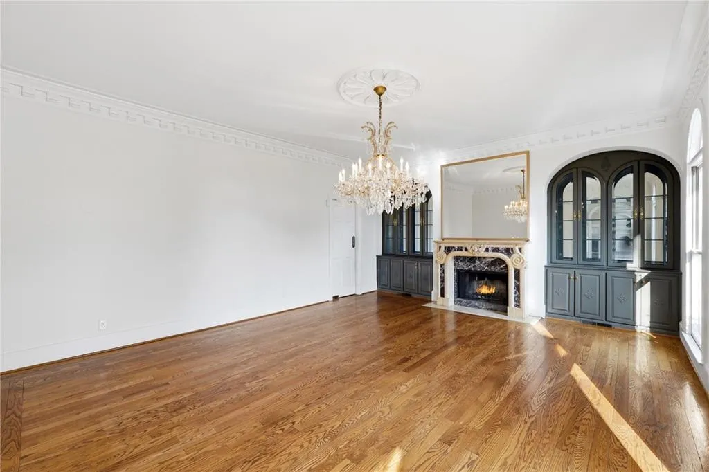 Unfurnished living room featuring a high end fireplace, suspended lighting, wood finished floors, and ornamental molding