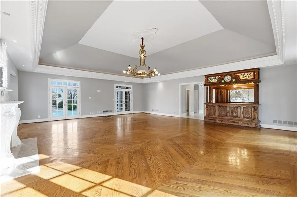 Unfurnished living room featuring parquet floors, suspended lighting, a tray ceiling, and ornamental molding