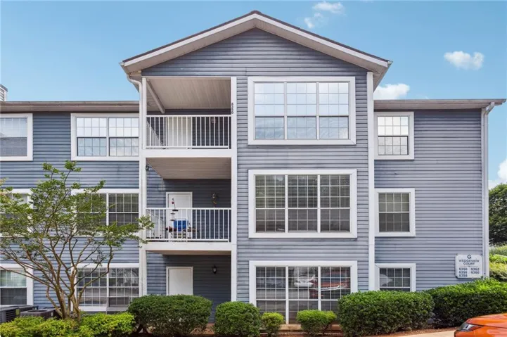 Three-story multifamily building with light blue siding, multiple windows, and two balconies with white railings