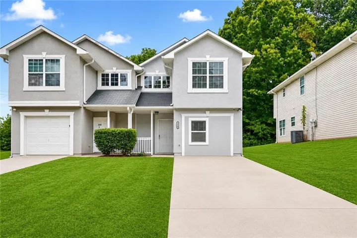 Contemporary townhome exterior featuring light gray stucco siding, white-framed windows, an attached single-car garage, and a covered porch entry