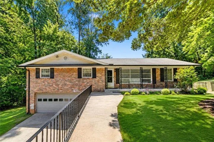 Brick facade residence with an attached garage, a paved driveway, and a front porch featuring an iron railing