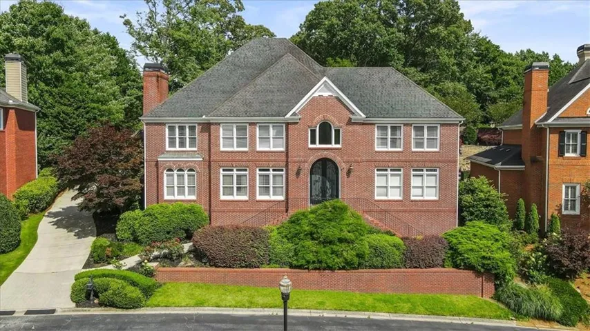 Brick exterior residence featuring a prominent gabled entrance, multiple white-trimmed windows, and a dark double-door entry