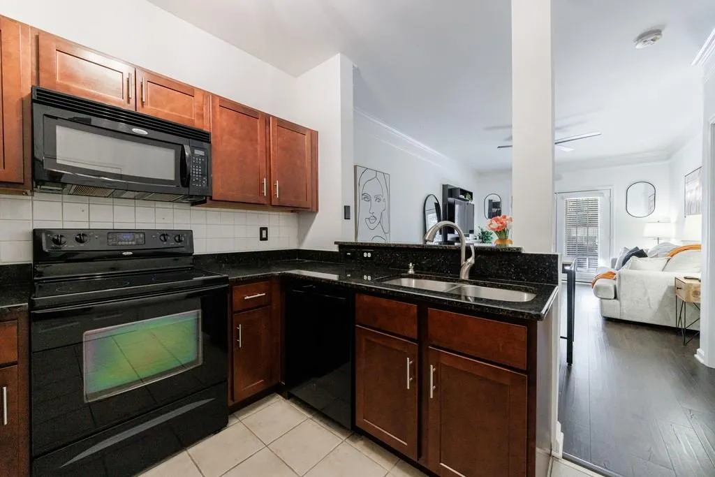 Kitchen featuring sink, kitchen peninsula, dark stone counters, decorative backsplash, and black appliances