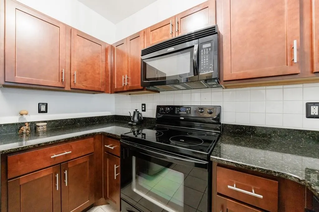 Kitchen featuring dark stone countertops, tasteful backsplash, and black appliances