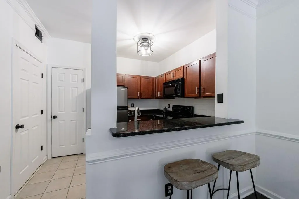 Kitchen featuring light tile patterned floors, black appliances, a kitchen bar, decorative backsplash, and kitchen peninsula