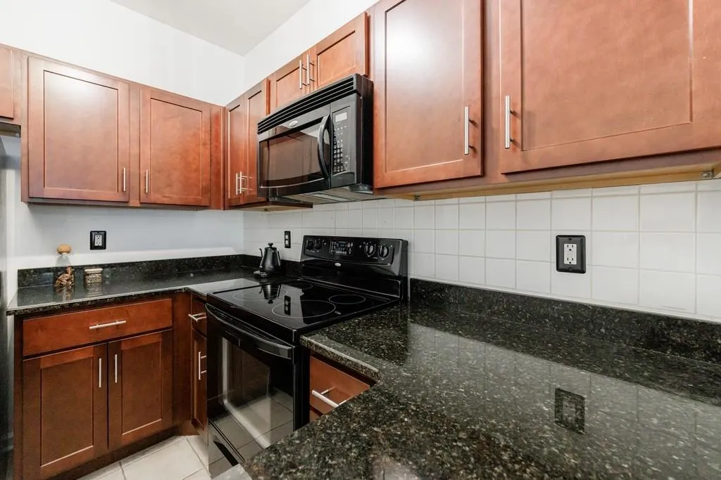 Kitchen featuring tasteful backsplash, dark stone countertops, light tile patterned floors, and black appliances