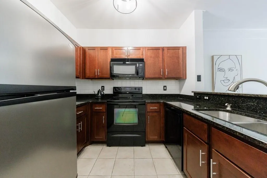 Kitchen with sink, light tile patterned floors, dark stone countertops, tasteful backsplash, and black appliances
